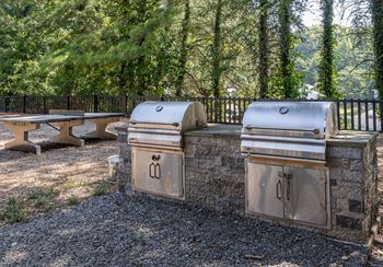 Three outdoor grills are lined up on a gravel area.